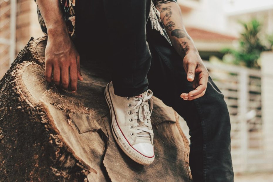 man sitting on log black pants and white converse sneakers
